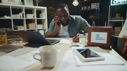 Portrait of busy afro manager writing notes on documents near laptop in office.