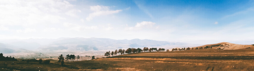 Obraz premium Georgian autumn landscape web banner. Sunny and bright November with trees and foggy mountains over horizon. Great for website banner advertisements