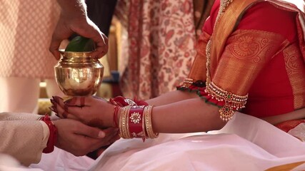 beautiful Indian bride and groom in ethnic clothes wearing gold jewellery doing religious rituals during wedding ceremony. close up hands shot. south indian bengali themed wedding.