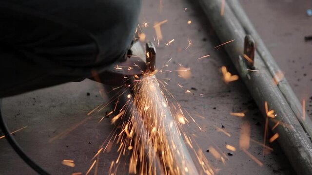 Remove excess weld metal in iron pipes and get the smooth finishing of the welding, using electric hand grinder by the handyman outdoor slow-motion clip, sparkes of particles coming towards the camera
