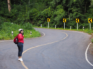 Asian tourist woman walking on winding road with curve warning sign in the forest