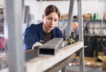Qualified focused workwoman inspecting shape of steel stocks in metal cutting workshop....