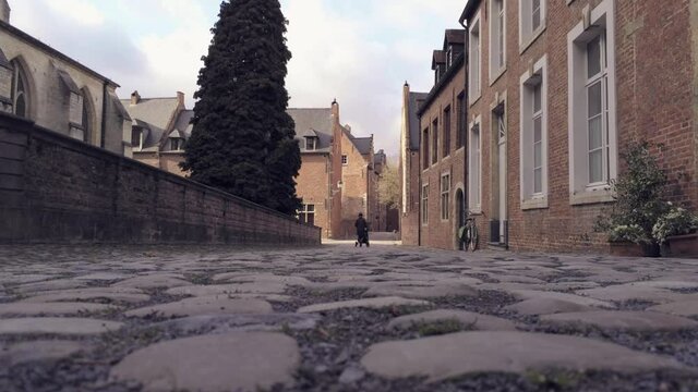 Woman with carriage walks at beguinage Groot Begijnhof in Leuven, Belgium. Low angle shot