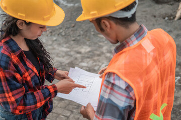 male and female asian contractors wearing safety helmets holding the site plan building during...