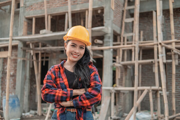 Naklejka na ściany i meble beautiful female asian contractors wearing safety helmets with crossed hands in the background of building construction