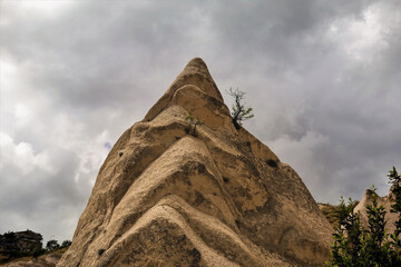 A strange spiky conical rock against a cloudy sky. On the slopes there are stone folds and a lonely...