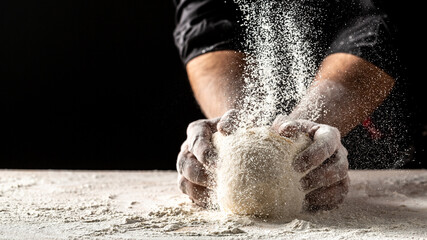 Hands of baker kneading dough isolated on black background. prepares ecologically natural pastries - obrazy, fototapety, plakaty