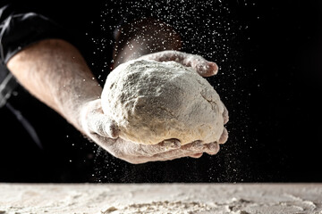 White flour flying into air as pastry chef in white suit slams ball dough on white powder covered...
