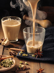 Masala tea with spices is poured into glass mugs on a wooden table.