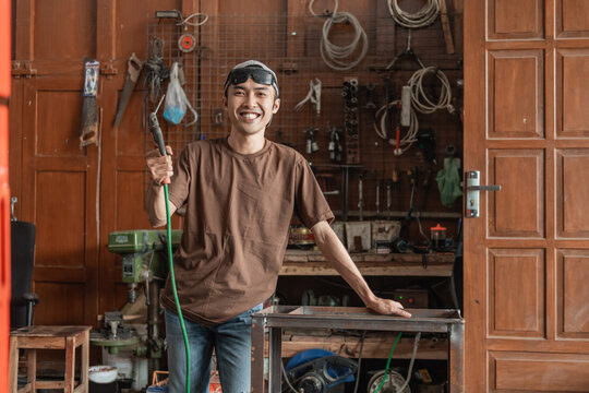 smiling welder looks into the camera while holding an electric welder in a welding shop