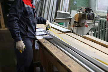 A photo of a worker measures a window sill with a tape measure for cutting on a miter saw....
