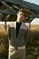 Portrait of young beautiful man in village area. Yellow field. Sun light, blue sky, autumn. Checkered pants, black shirt and jacket