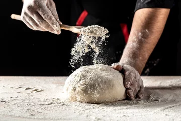 Deurstickers chef in a professional kitchen prepares the dough with flour, Beautiful and strong men's hands knead the dough from which they will then make bread, pasta or pizza © Надія Коваль