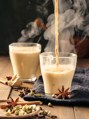 Masala tea with spices is poured into glass mugs on a wooden table.
