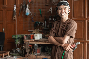 Male welder smiles with crossed hands while holding electric welder in welding workshop background