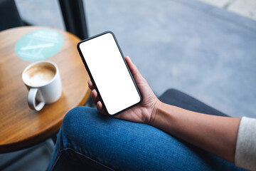 Mockup image of a woman holding mobile phone with blank white desktop screen with coffee cup on the table