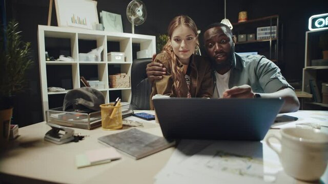 Flirting afro man hugging beautiful lady near laptop in hipster office.