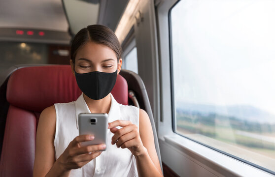 Asian business woman using mobile phone during commute to work in public transport train wearing face mask for corona virus prevention.