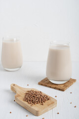 Buckweat in form of seeds on cutting board and glass of gluten-free milk which is source of protein, essential amino acids, calcium, manganese and vitamins on white wooden background. Vertical