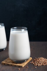 Buckwheat in form of seeds and glass of gluten-free milk which is source of protein, amino acids, manganese and vitamins for healthy dieting on dark wooden table against black background. Vertical