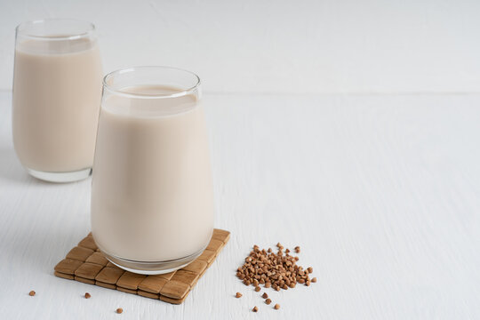Buckwheat seeds and glass of gluten-free milk which is source of protein, amino acids, manganese and vitamins for healthy dieting on white wooden background at kitchen. Image with copy space
