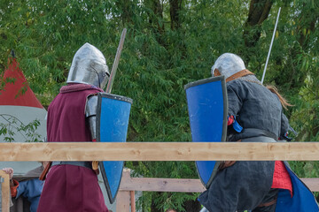 Two foot warriors in heavy medieval armor fight in the arena. Armed with swords. They are protected...