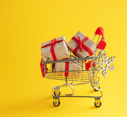 Shopping cart with Christmas gifts on yellow background. Concept of Christmas, New Year shopping and sales. - 393019239