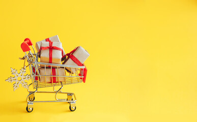 Supermarket stroller with Christmas gift boxes on yellow background with copy space. - 393019243
