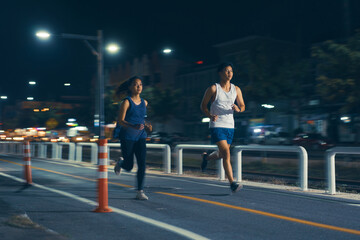 Asian couple jogging in the city streets at night.