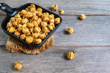 Flat lay of tasty caramel popcorn in black ceramic pan plate with sack table cloths on wooden table, close up.