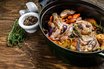 Baked whole goat shoulder leg in a baking dish.  Wooden background. Top view. Copy space