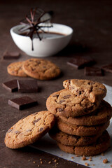 Chocolate chip cookies on a table with chocolate pieces and chocolate sauce in the background