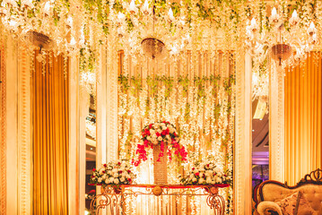 table of three decorated bouquets of white and pinks flowers with strings of flowers hanging and light of three bright warm chandeliers glowing the decoration at an Indian wedding party stage.