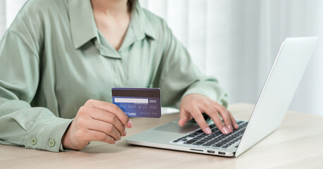 The businesswoman's hand is holding a credit card and using a laptop for online shopping and internet payment in the office