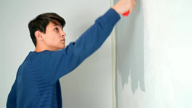 A hearing-impaired young man in hearing aids paints the wall with a roller gray. 4k