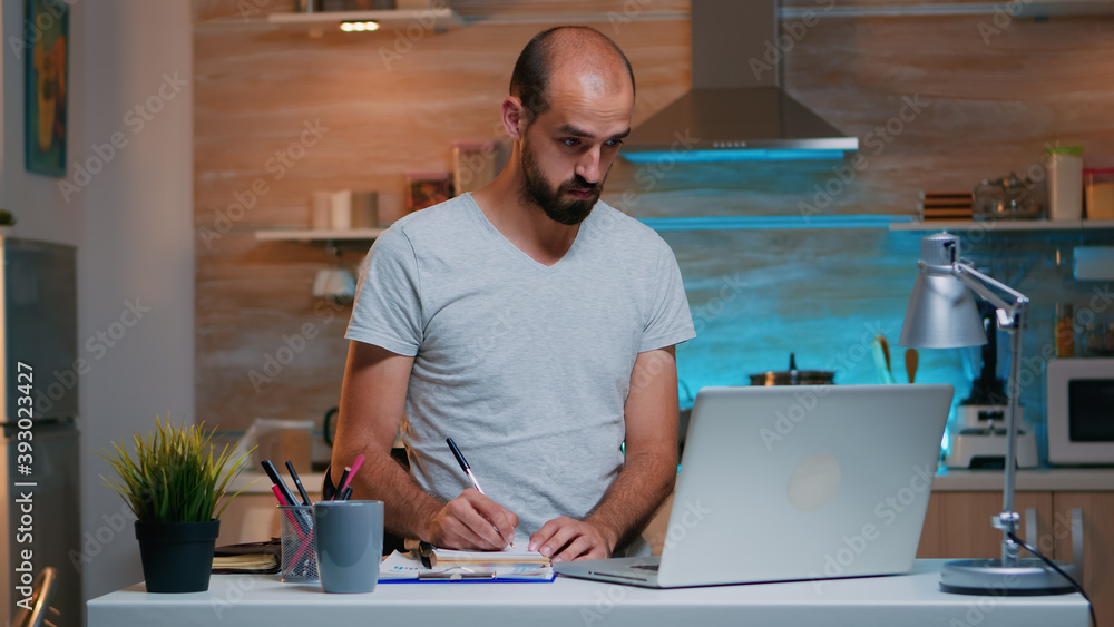 Poster freelancer writing notes in notebook while studying and using modern technology working at home over