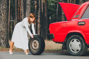 Obraz na płótnie Canvas Chernigov, Ukraine - November 10, 2020: Girl in a wedding dress rolls the wheel. Vaz 2101. Red retro car in the forest