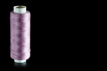 Reel with pink sewing silk threads isolated on a black background, close-up, copy space. Bright background for sewing and needlework