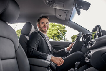 Smiling bearded male sitting at driver's seat, holding steering wheel