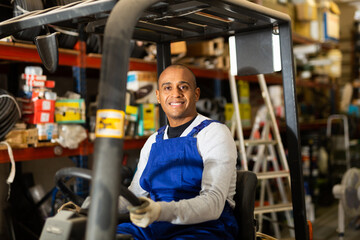Cheerful Latin American worker of building materials warehouse working on forklift truck
