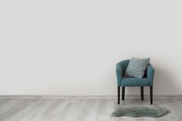 Stylish armchair with pillow near light wall in room