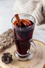 Mulled wine with a stick of cinnamon, spices in a glass on a wooden stand with a knitted jacket in the background.