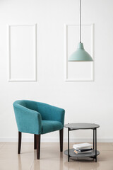Stylish armchair with table and books near light wall in room