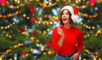 winter holidays and people concept - happy smiling young woman in santa helper hat with candy canes over christmas tree lights background