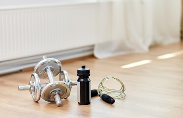 Obraz na płótnie Canvas sport, fitness and objects concept - dumbbells, skipping rope and bottle on floor at home