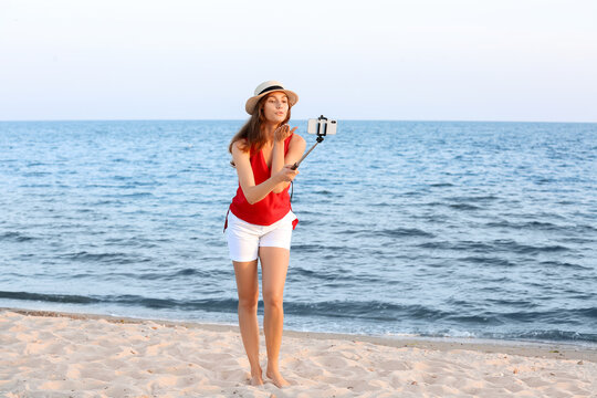 Beautiful young woman taking selfie on sea beach