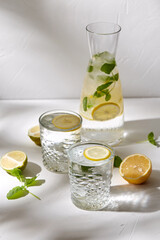 drink, detox and diet concept - glasses with fruit water or lemonade, lemons, limes and peppermint on white table