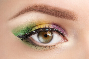 Gold, purple and green Mardi gras makeup. Woman eye with bright eyeshadows and rhinestones on false eyelashes macro