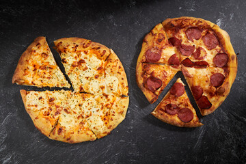 Pizza on black stone background, top view. Pepperoni Pizza and Ultimate Cheese Pizza with Cheddar Mozzarella Ricotta Parmesan Cheese