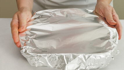 Chef wraps baking pan with aluminum foil. Baking process